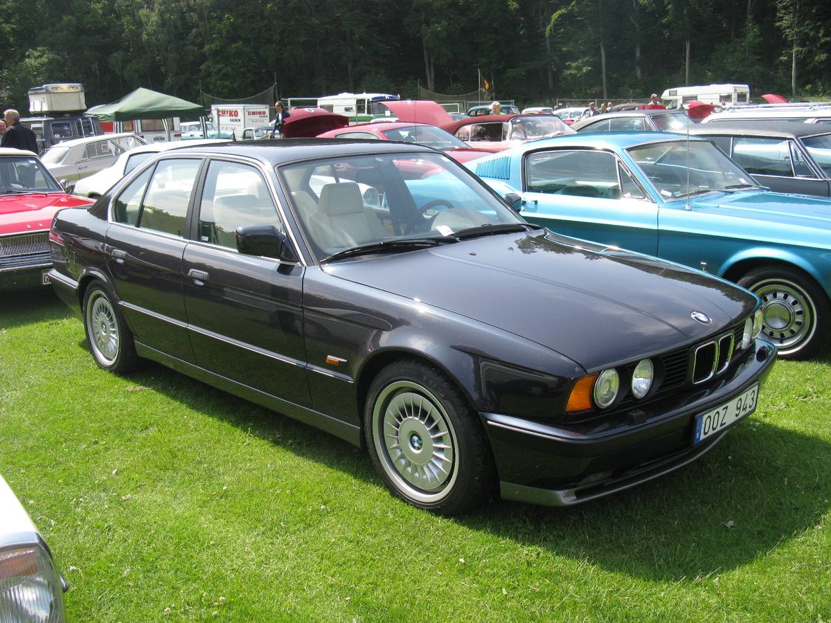Tmavá BMW M5 řady E34 na trávě, vidět je přední kolo s lopatkovým krytem M System