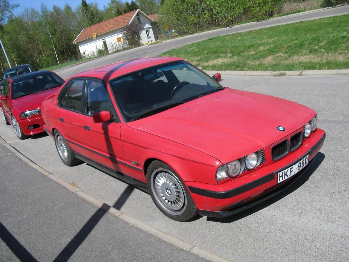 Červený sedan BMW řady E34 zaparkovaný u silnice