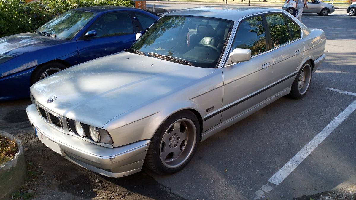 Šedý sedan BMW řady 5 generace E34 zaparkovaný u chodníku