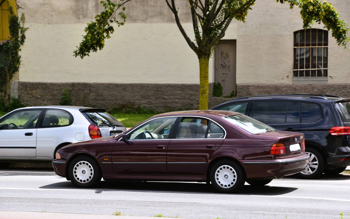 Vínově červený sedan BMW E39 520i z boku a zezadu, se zadními světly u kufru