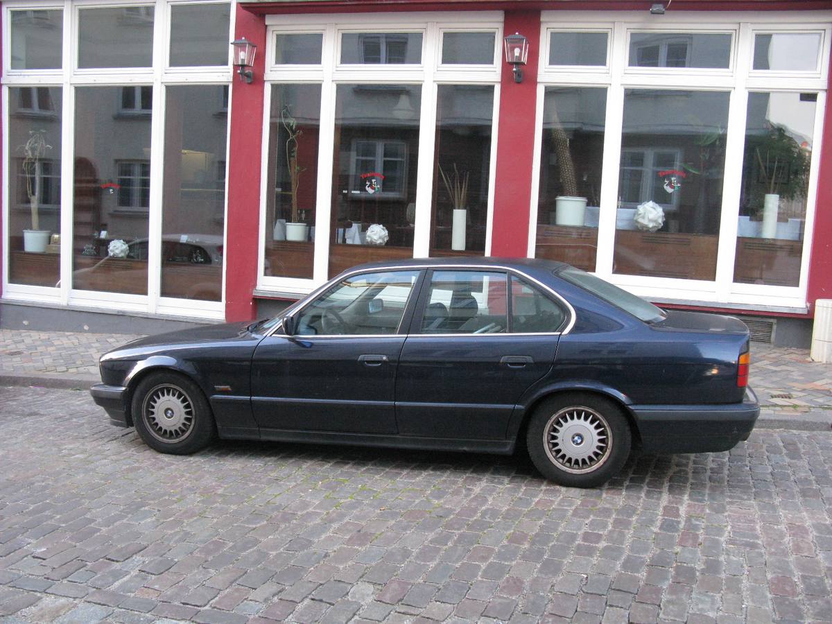 Tmavě modrý sedan BMW řady 5 generace E34 zaparkovaný u chodníku