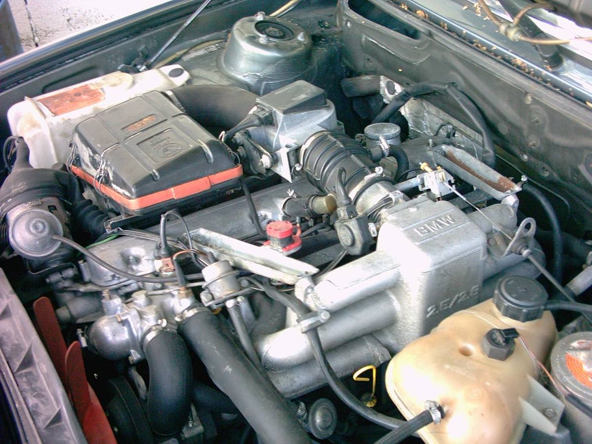 Motorový prostor BMW E28 se šestiválcem M30, sacím potrubím s nápisem 2.5/2.8 a měřičem vzduchu