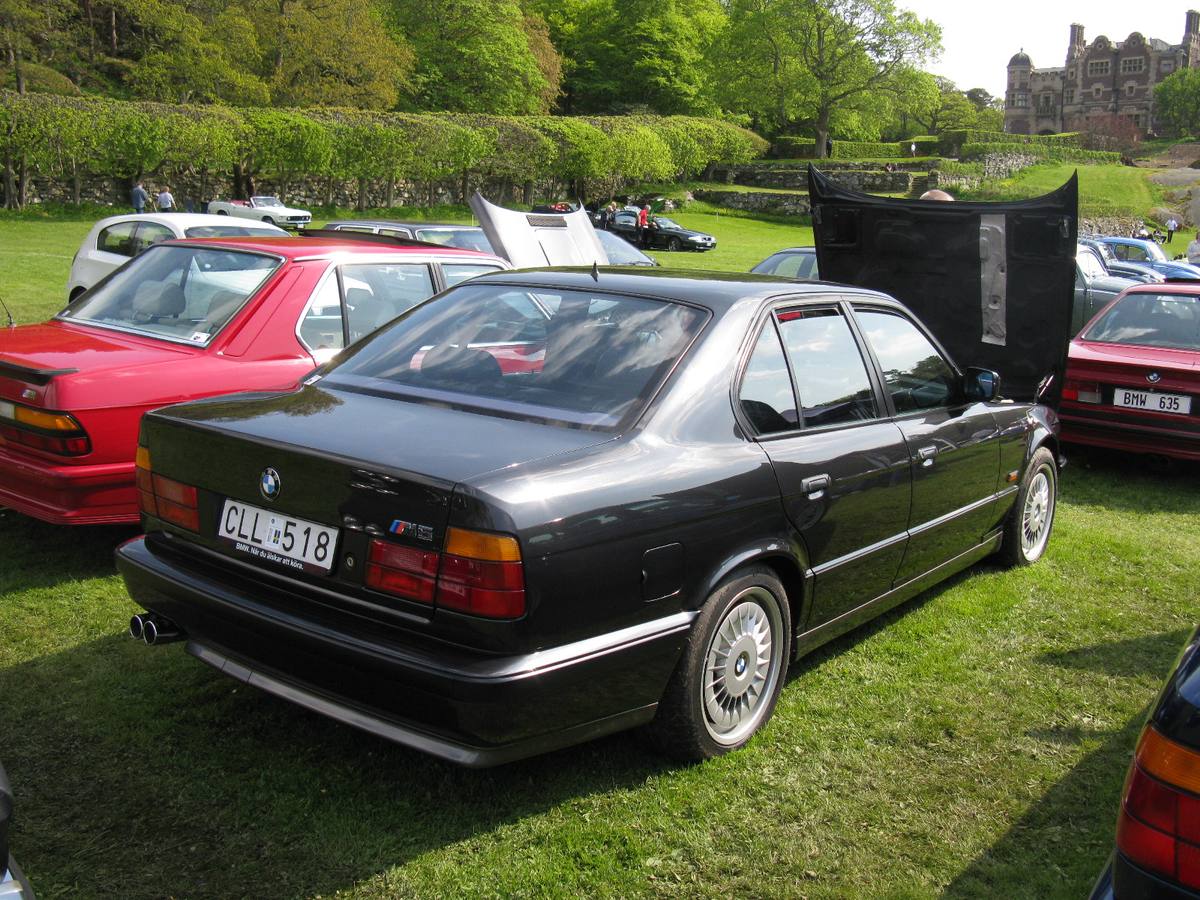 Tmavá limuzína BMW M5 řady E34 zezadu, na zadním kole kryt kol M System I