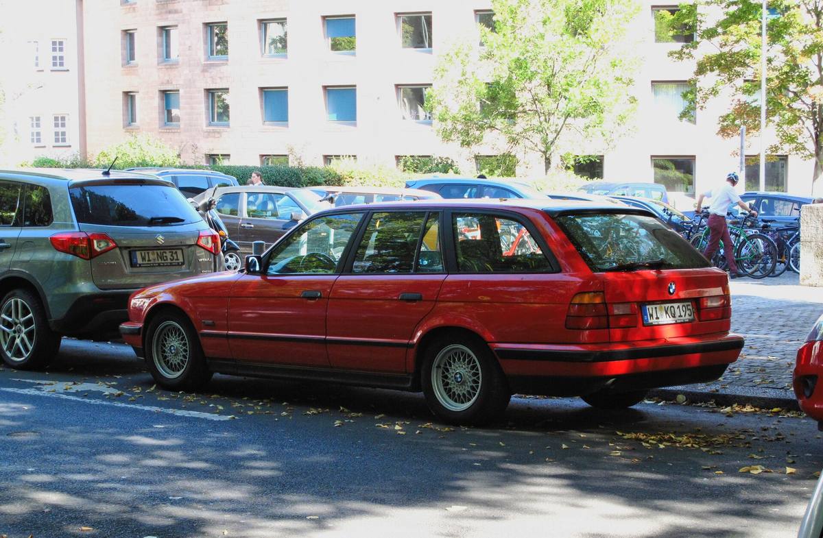 Červené kombi BMW řady 5 generace E34 zaparkované u chodníku