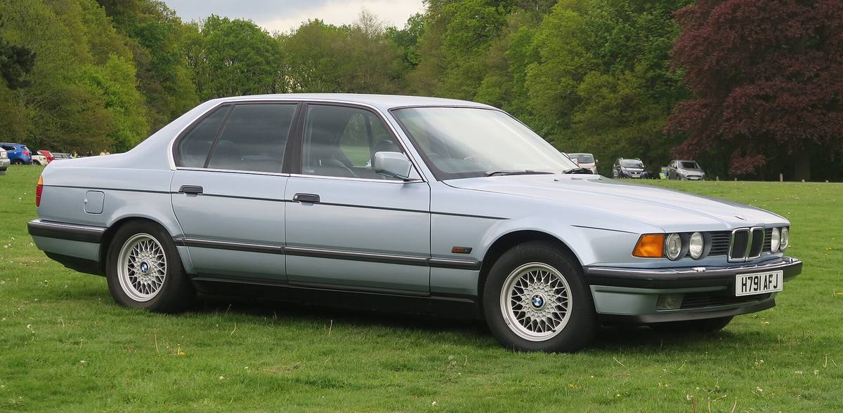 Světle modré BMW 730i řady E32 zaparkované na travnaté ploše