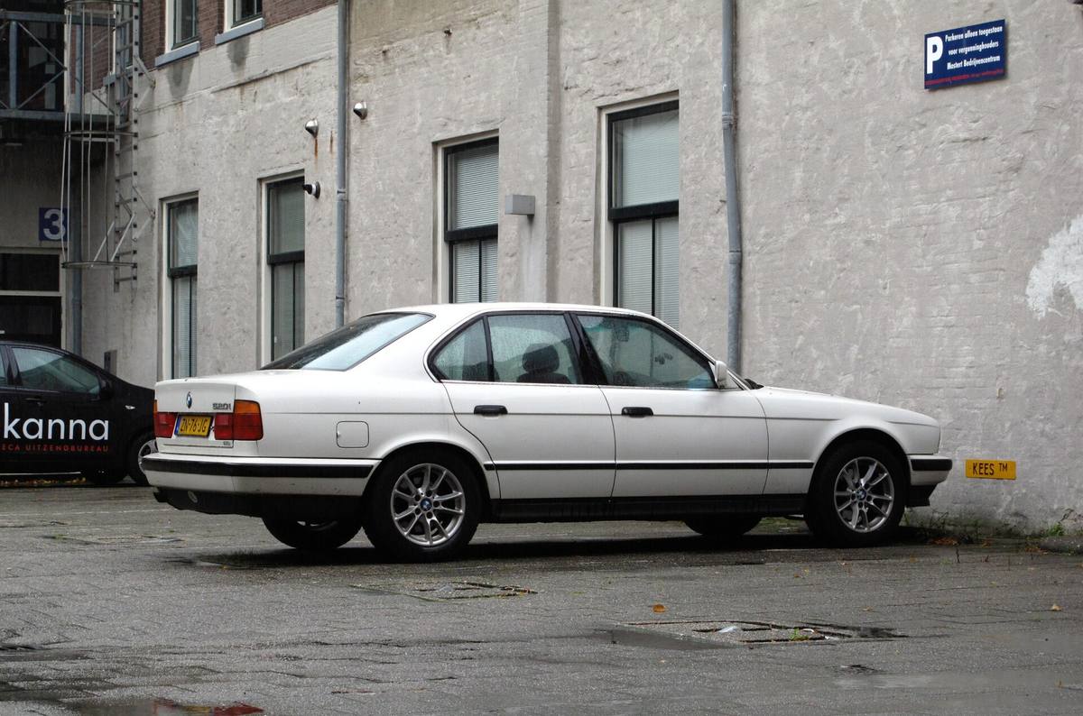 BMW 520i generace E34 zprava, tmavý sedan zaparkovaný u chodníku