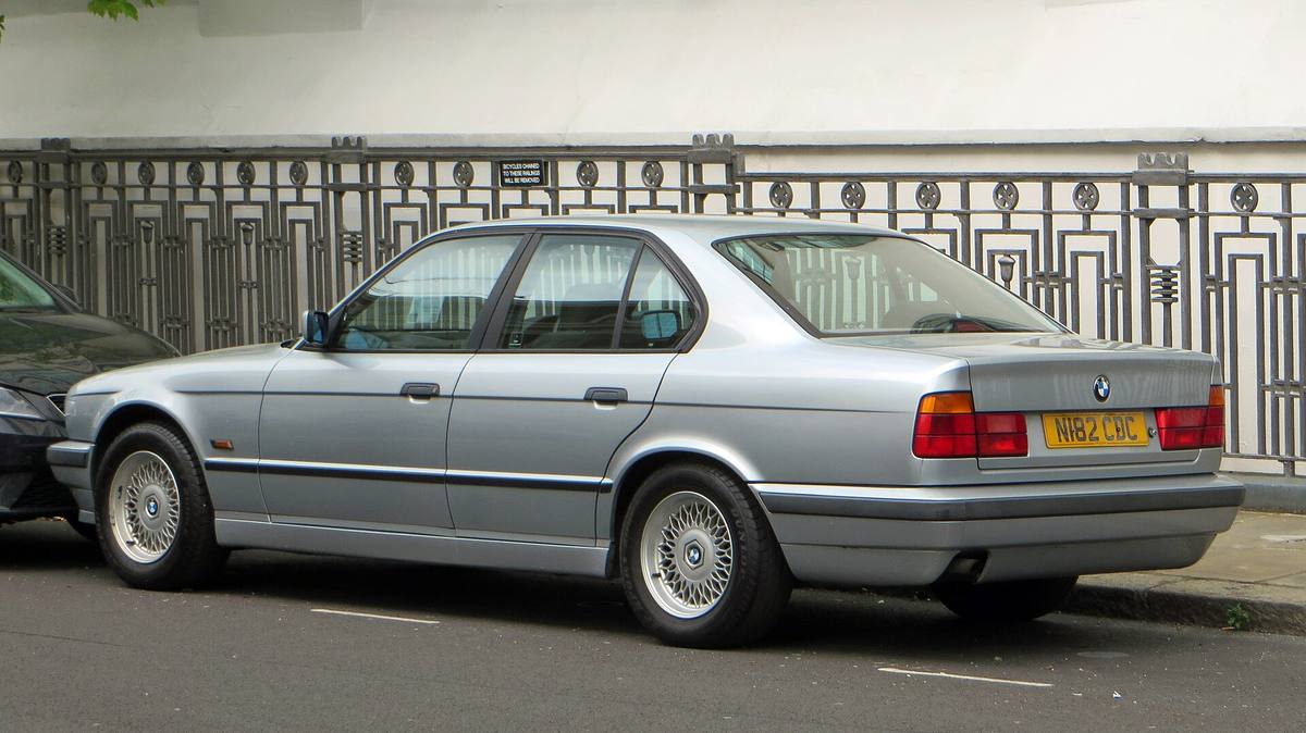 Stříbrné BMW 518i řady E34 z roku 1996 zaparkované u zábradlí, pohled zezadu z boku