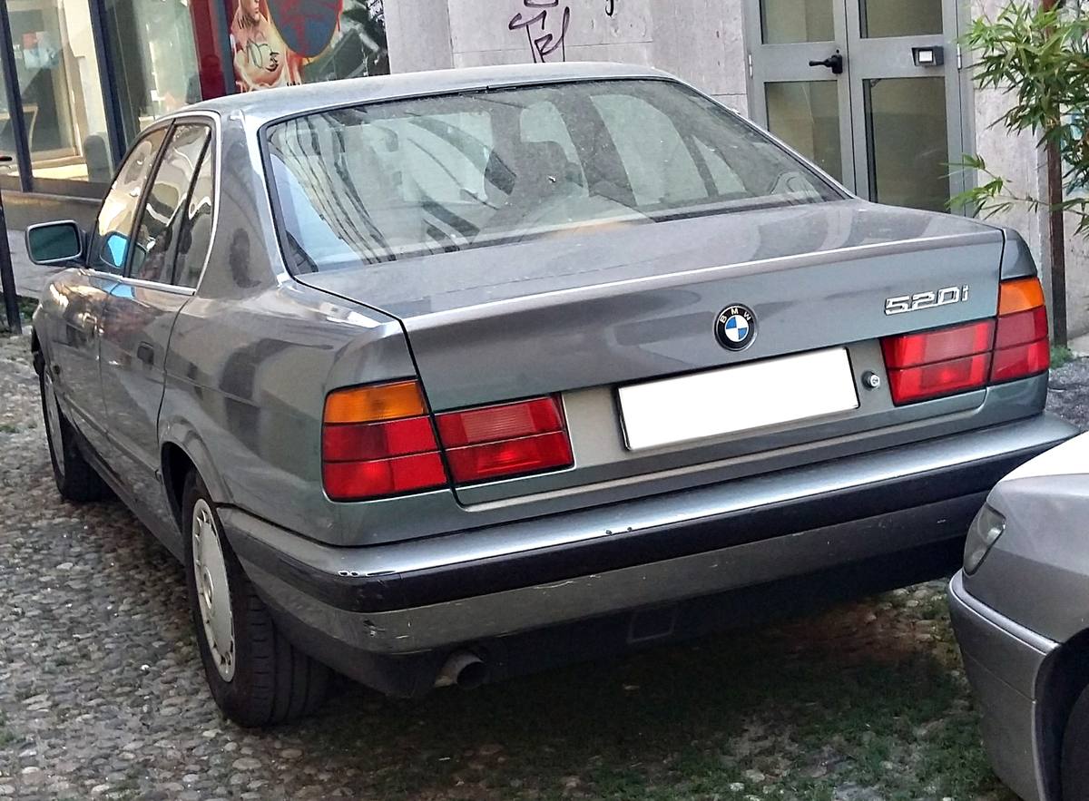Záď sedanu BMW E34 s nápisem 520i a kulatým odznakem na víku kufru